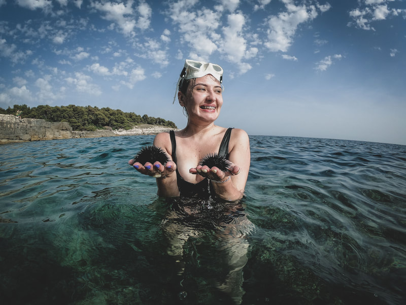 A happy girl joyfully holding two sea urchins in her hand, showcasing her exciting underwater discovery