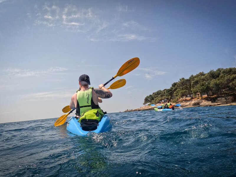 Kayaker enjoying a serene paddle on calm waters, surrounded by beautiful nature and clear blue skies.