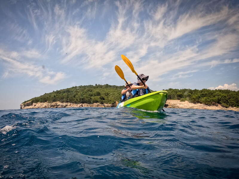 Two kayakers paddling along the picturesque coastline of Pula, surrounded by clear blue waters and rocky cliffs.